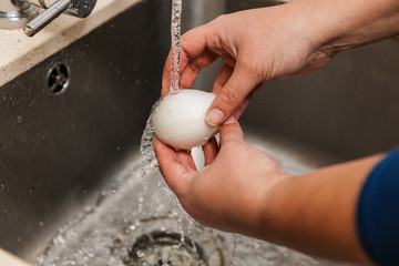 manos cogiendo cebolla pelada bajo el grifo para lavarla en agua en la pica