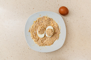 cocinando la receta de huevos rellenos de atún y mayonesa. en un plato se ve la mezcla y encima dos mitades de huevo con el relleno. al lado hay un huevo con cáscara