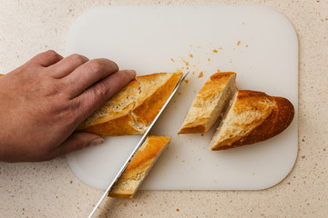pan baguette de harina cortado a cuchillo encima de tabla de corte, en mármol claro.