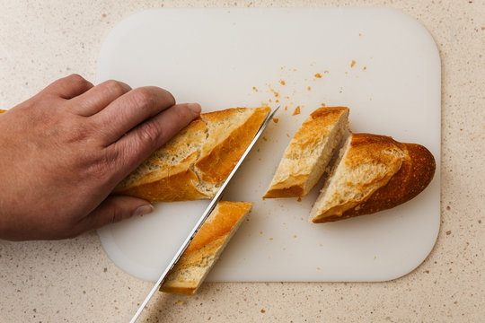 pan baguette de harina cortado a cuchillo encima de tabla de corte, en m&aacute;rmol claro.