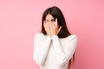 Young woman over isolated pink background covering eyes and looking through fingers