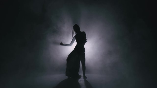 Silhouette dancer woman performing dance figures in fog. 4K Slow motion footage.