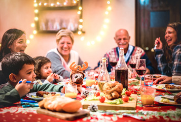 Fototapeta na wymiar Multi generation big family having fun at christmas supper party - Winter holiday x mas concept with grand parent and children eating together at home dinner - Focus on dog puppy toy with reindeer hat