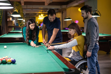 Disabled girl in a wheelchair playing billiards with friends