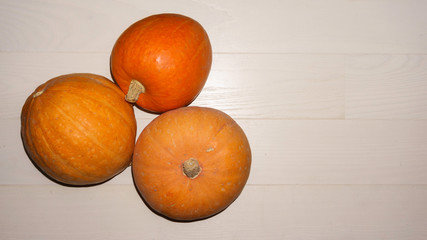 Three yellow ripe pumpkin on a wooden light background. For pumpkin carving ideas. Flat lay with copy space. Top view.