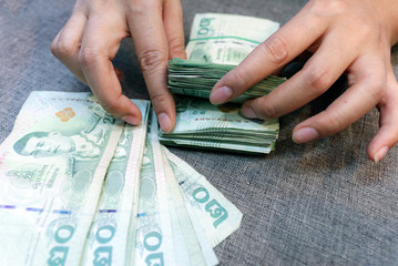 The woman's hand is counting twenty Thai baht banknotes.