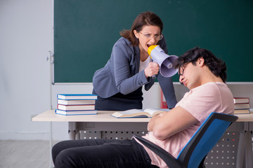 Old female teacher and male student in the classroom