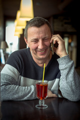 Cheerful man in a sweater talking on a mobile phone in a cozy cafe and laughing. Pleasant conversation over a Cup of tea. Concept of modern technologies and mobile communication