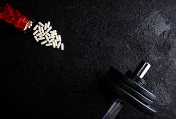 Naklejka premium Sports supplements with weights on dark background. Medicines