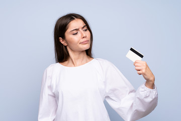 Fototapeta premium Young woman over isolated blue background holding a credit card
