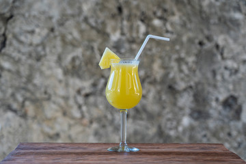 Freshly squeezed juice from pineapple in a glass goblet on the background of an old stone wall