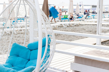 Modern design white luxury hanging rattan wicker chair egg form with cozy blue pillows inside on the beach