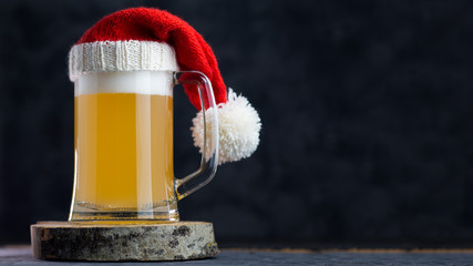 Glass Christmas beer mug in Santa hat on black background with copy space