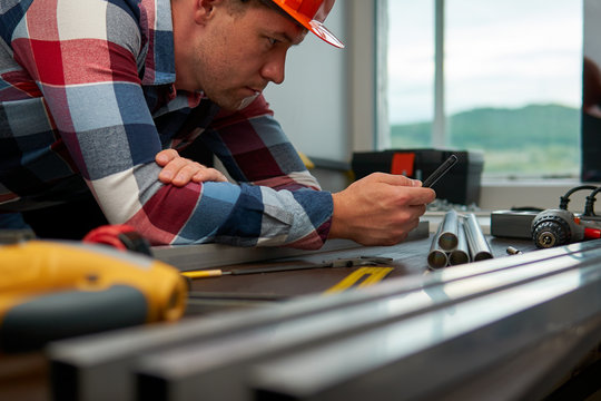 Young guy engineer in a plaid shirt makes calculations using a smartphone.