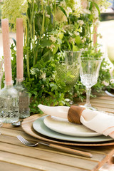 Festive table decor in openair next to the pond. Green color with wooden cutlery. Different natural white flowers. Wooden table and chairs. Wine glasses. Luxury wedding, party, birthday.