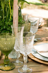 Festive table decor in openair next to the pond. Green color with wooden cutlery. Different natural white flowers. Wooden table and chairs. Wine glasses. Luxury wedding, party, birthday.