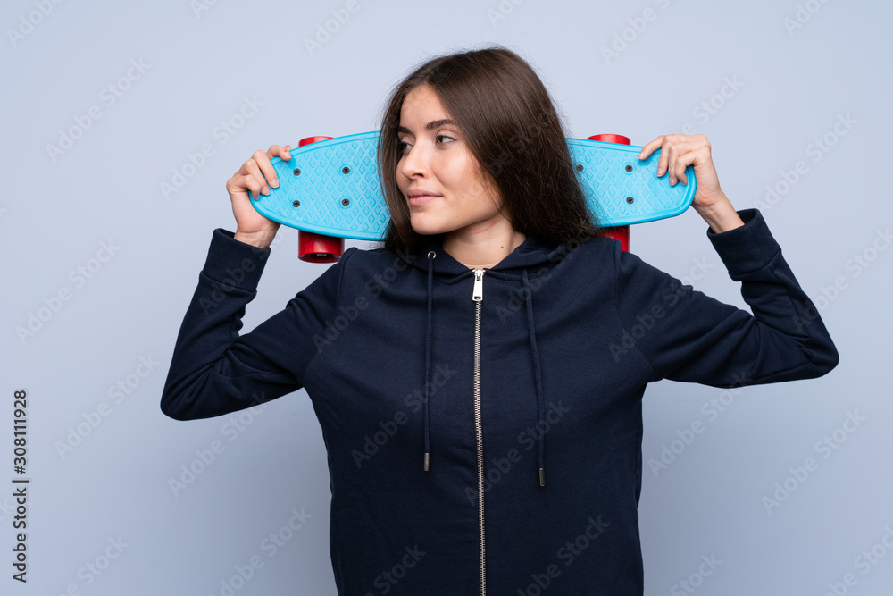 Wall mural Young woman over isolated blue background with skate and looking side