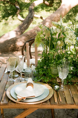 Festive table decor in openair next to the pond. Green color with wooden cutlery. Different natural white flowers. Wooden table and chairs. Wine glasses. Luxury wedding, party, birthday.