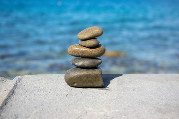 Fototapeta na wymiar Five stones cairn tower, rock zen sculpture, brown beige pebbles and sea light blue background