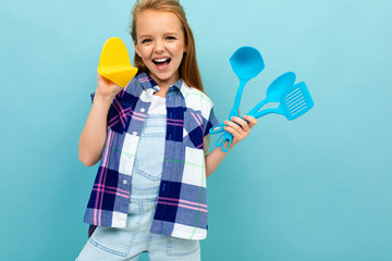 smiling european girl with cooking utensils in hands on a light blue wall