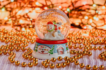 Christmas glass sphere with a snowman and snow inside on a blurry background with lights.