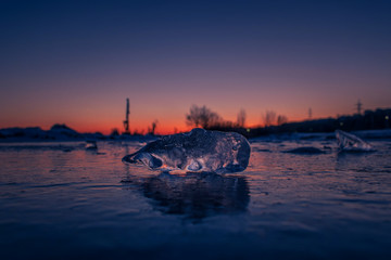 A piece of clear ice close up on frozen water at sunset