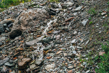 Clear spring water flows on beautiful stony steep slope. Boulder stream with small mountain creek. Many wet stones on mountainside. Nature background with highland brook close-up. Clear water stream.