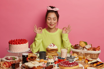Beautiful Asian woman sweet tooth meditates and practices yoga, eats yummy pancakes and cakes, feels relaxed, going to taste birthday cake, loves desserts, gets much calories. Junk food concept