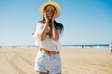 girl laughs and joyfully put her hands to her cheeks, stands on a sandy beach