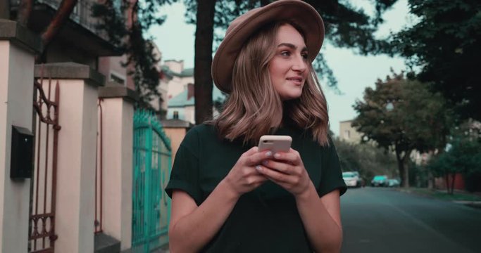 Portrait of Smiling woman walking in the City while Typing Messages on her Smartphone. Looking Happy and Smiling. Having fun. Looking at mobiles screen. Attractive girl