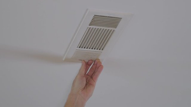 Handyman adjusting HVAC ceiling air vent. Air flow adjustment for overhead home heat and air conditioning ventilation duct.