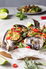 Baked dorado or sea bream fish with lime, chilly, herbs and vegetables, light grey stone background. Selective focus. Keto diet. Comfort food.