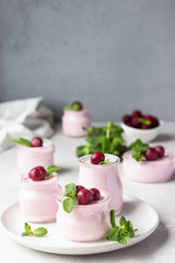 Delicious Italian dessert cherry panna cotta with fresh cherries and mint in jars. Light grey stone...