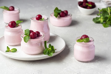 Delicious Italian dessert cherry panna cotta with fresh cherries and mint in jars. Light grey stone background, selective focus. Copy space.