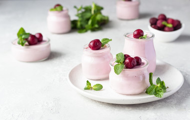 Delicious Italian dessert cherry panna cotta with fresh cherries and mint in jars. Light grey stone background, selective focus. Copy space.