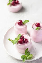 Delicious Italian dessert cherry panna cotta with fresh cherries and mint in jars. Light grey stone background, selective focus. Copy space.