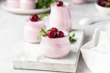 Delicious Italian dessert cherry panna cotta with fresh cherries and mint in jars. Light grey stone background, selective focus. Copy space.