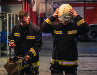 Portrait of two young firemen in uniform standing inside the fire station .