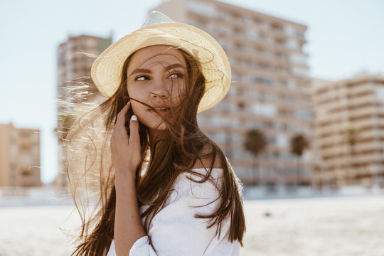 girl in a hat with long hair fluttering from the wind looks with interest and slightly wary over her shoulder