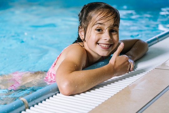 Portrait  little girl having fun in  indoor swimming-pool. The girl is resting at the water park. Active happy kid. Swimming school for small children. Concept friendly family sport and summer vacatio