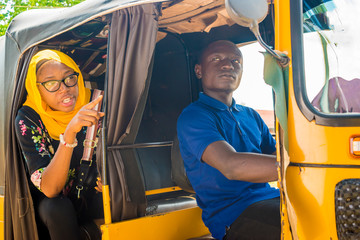 african man driving a auto rickshaw taxi being annoyed by a female passenger who's talking to him