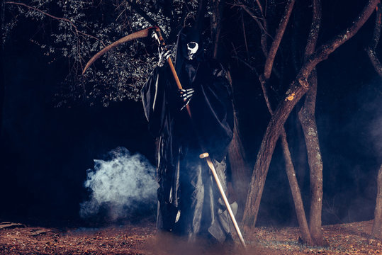 Portrait of grim reaper, the angel of death ( Azrael ) lurking through the woods at night surrounded with mist, smoke in a mystical forest holding his shythe.