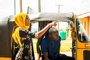 young african woman giving directions to the driver of an auto rickshaw taxi, pointing in the...