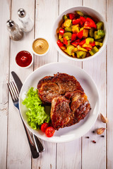 Grilled steak and vegetables on wooden background