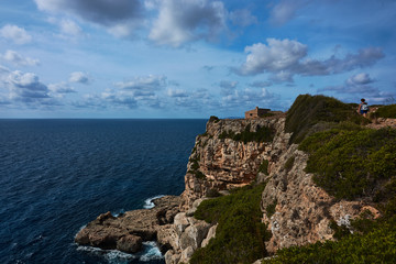 Fototapeta na wymiar Cliffs and small house by the sea. Hiker walking. Blue sky with clouds. Mallorca, Spain