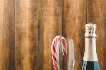 Bottle with sparkling wine and red caramel in glassware. Copy space. Wooden background. Christmas and New Year celebration.