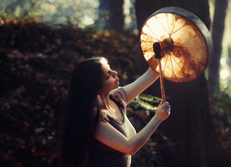 beautiful shamanic girl playing on shaman frame drum in the nature.