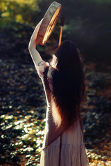 beautiful shamanic girl playing on shaman frame drum in the nature.