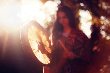 beautiful shamanic girl playing on shaman frame drum in the nature.