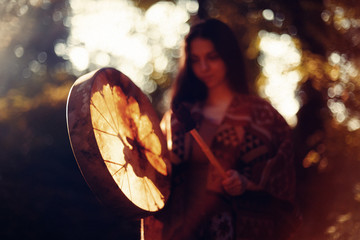 beautiful shamanic girl playing on shaman frame drum in the nature.